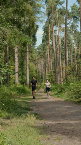 Video-Vertical-De-Una-Pareja-Haciendo-Ejercicio-Al-Aire-Libre-Corriendo-Por-Una-Pista-A-Través-Del-Bosque-Hacia-La-Cámara-Con-Ropa-Deportiva-Filmada-En-Tiempo-Real-3